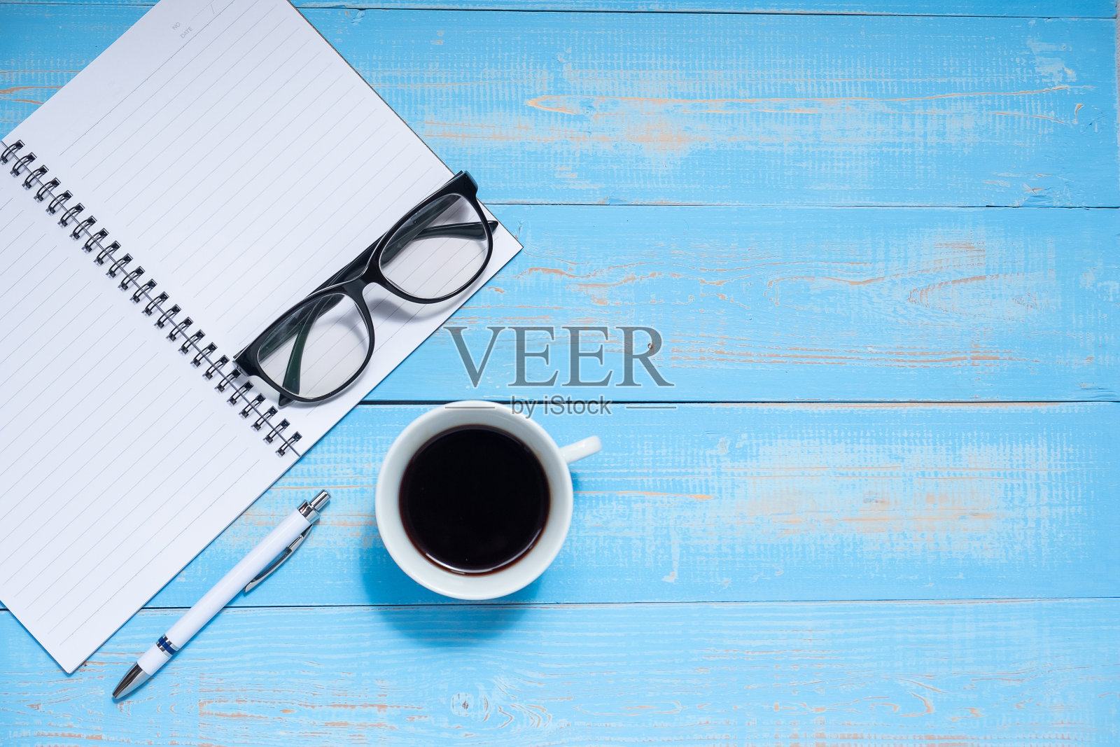 一杯黑咖啡和办公用品;蓝色木桌背景上有钢笔、笔记本和眼镜。顶部视图与复制空间照片摄影图片