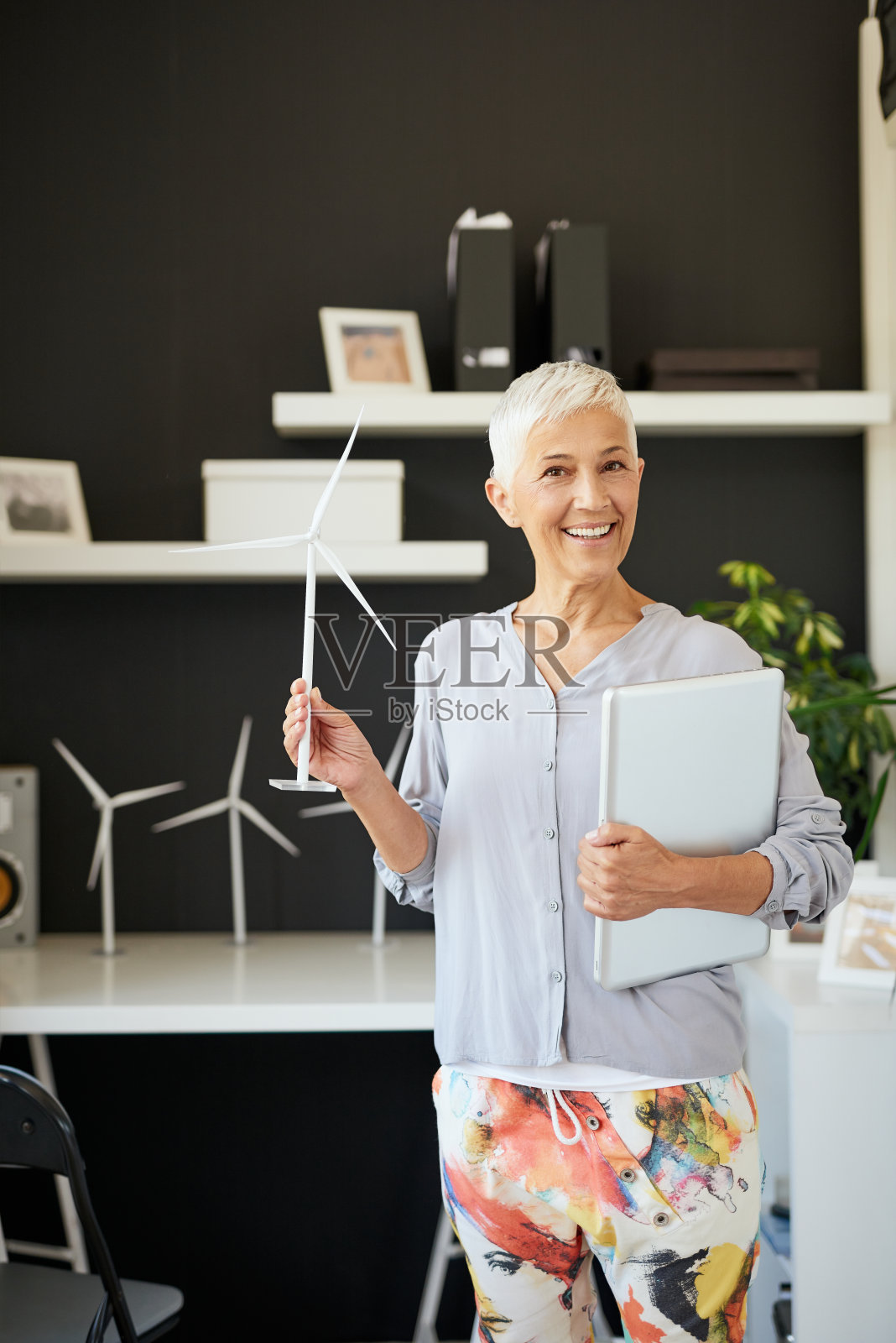 女人站在办公室里拿着风车模型和笔记本电脑。照片摄影图片