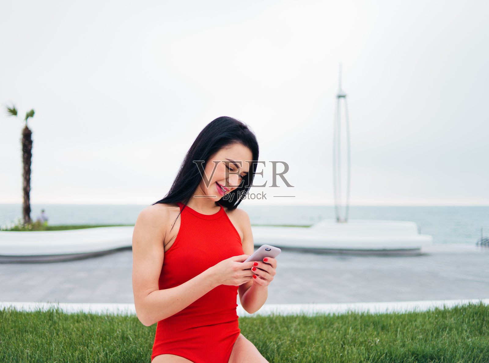 开朗迷人的黑发女人在红色泳装聊天在户外的海滩上智能手机照片摄影图片