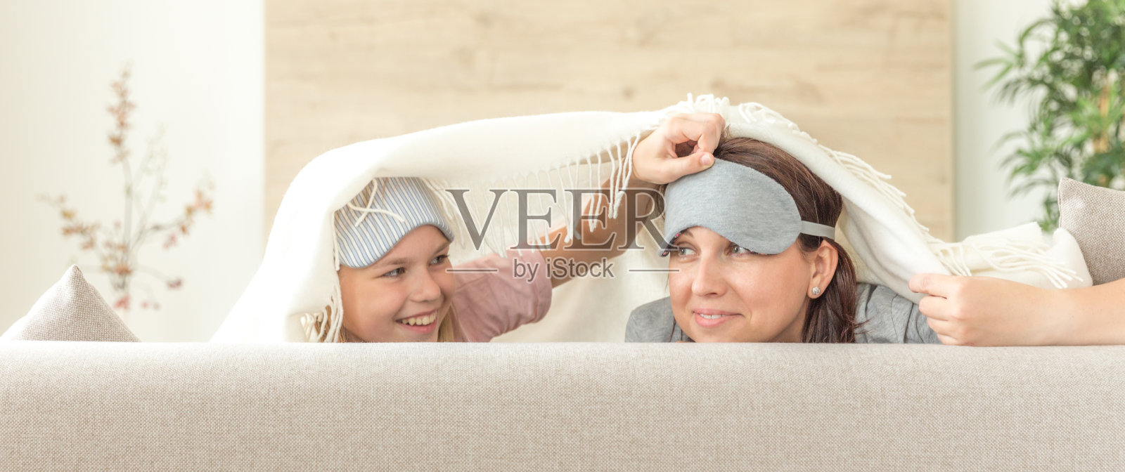 母亲和女儿幸福的家庭观念。戴着睡眠面罩，在客厅的沙发上玩耍照片摄影图片