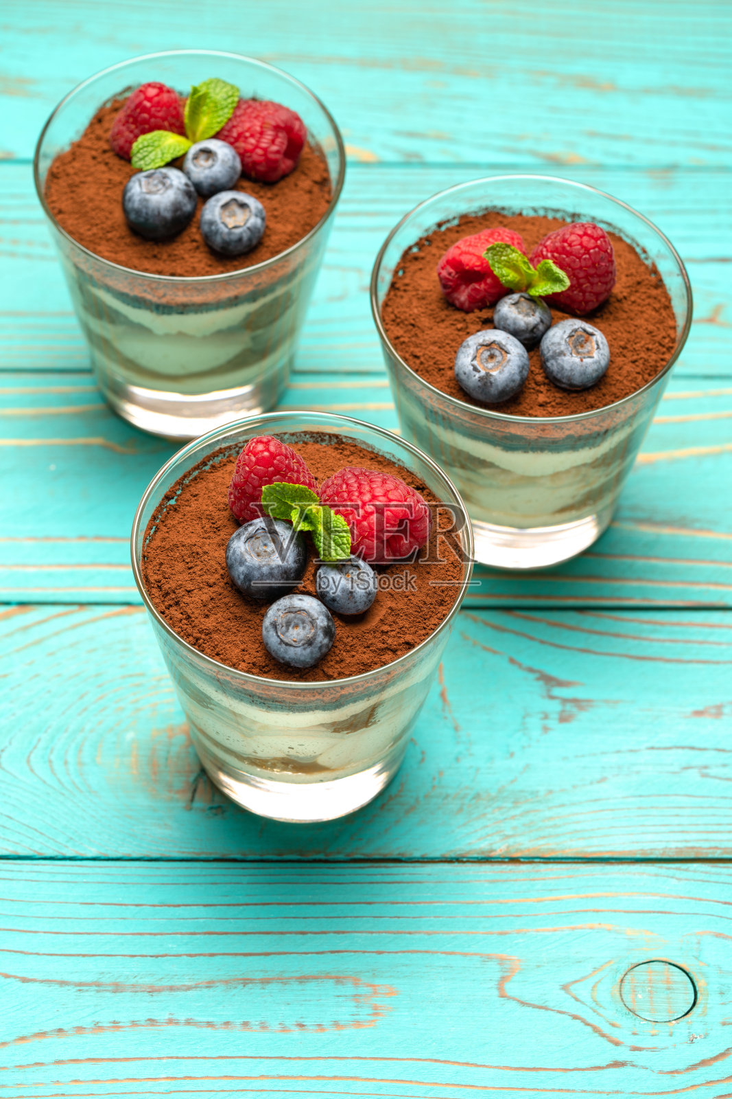 经典的提拉米苏甜点，蓝莓和草莓放在玻璃杯里，木质背景照片摄影图片