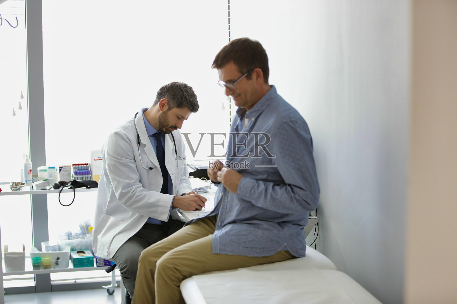 医生阅读医疗报告，而病人脱衣检查在医院照片摄影图片