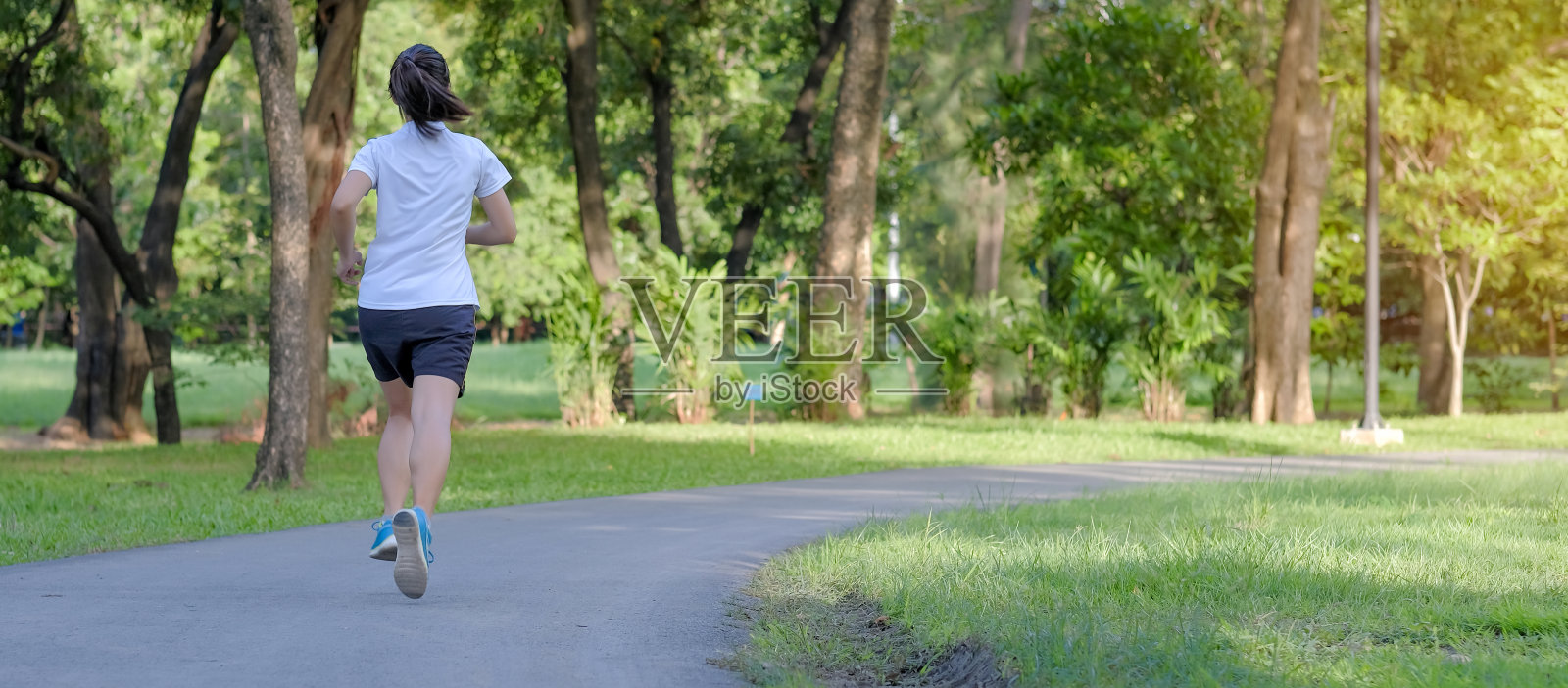 年轻的健身女性在公园户外跑步，女性跑步者在外面的道路上行走，亚洲运动员在阳光下慢跑和锻炼的人行道上早晨。运动、健康和健康的概念照片摄影图片