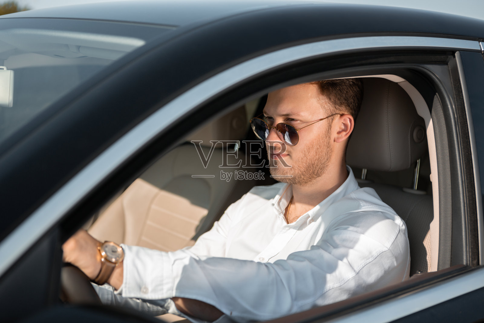 穿着白衬衫，戴着太阳眼镜的快乐司机开着他的豪华车。照片摄影图片