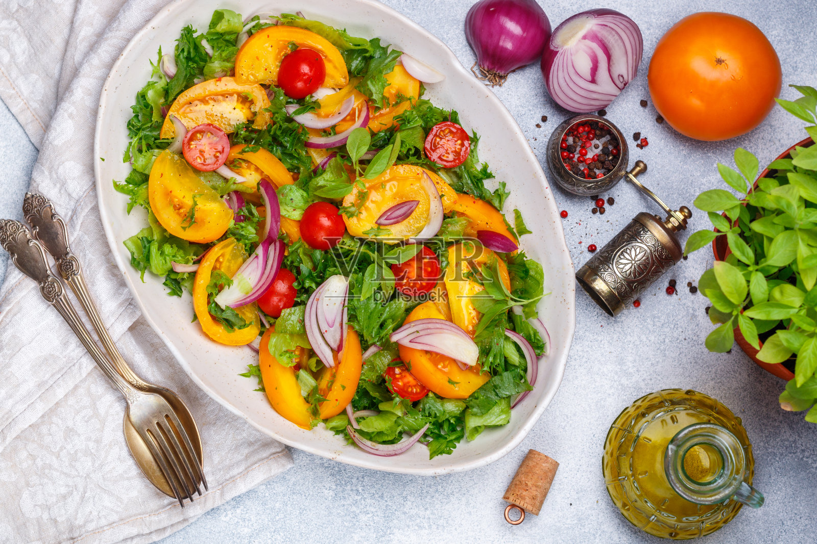 新鲜的蔬菜沙拉，色彩丰富的西红柿(樱桃，黄色和橙色)，红洋葱，生菜和罗勒香料和橄榄油在一个白色的盘子里。有选择性的重点照片摄影图片