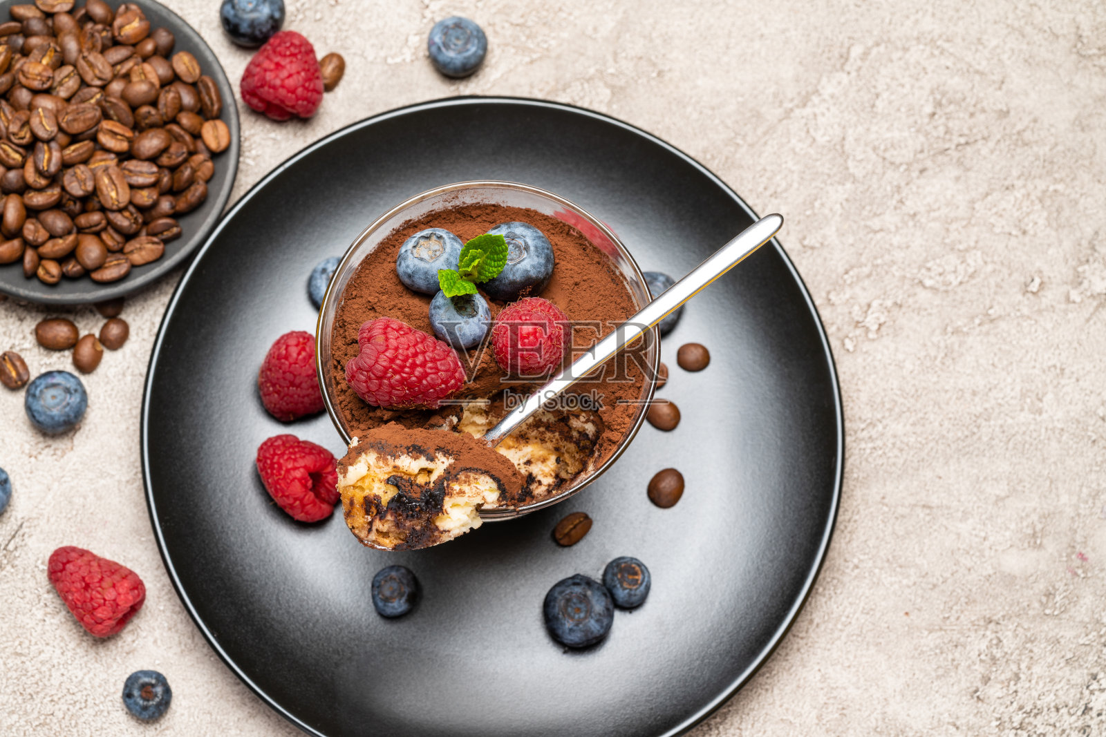 经典的提拉米苏甜点配蓝莓和覆盆子放在玻璃杯里，背景是混凝土照片摄影图片