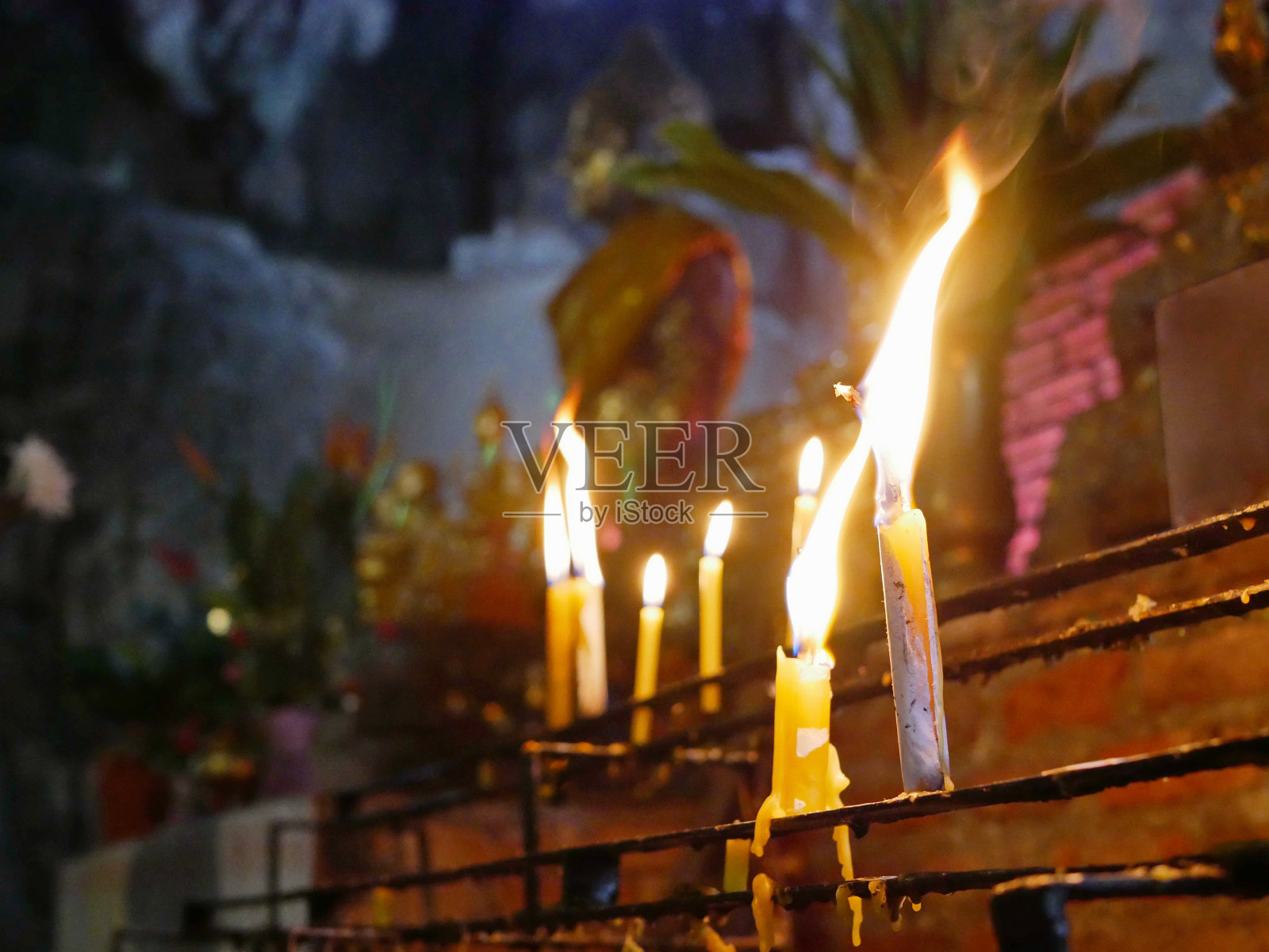 有选择地聚焦在一个架子上燃烧的蜡烛，背景是一尊佛像坐在一个深洞里照片摄影图片