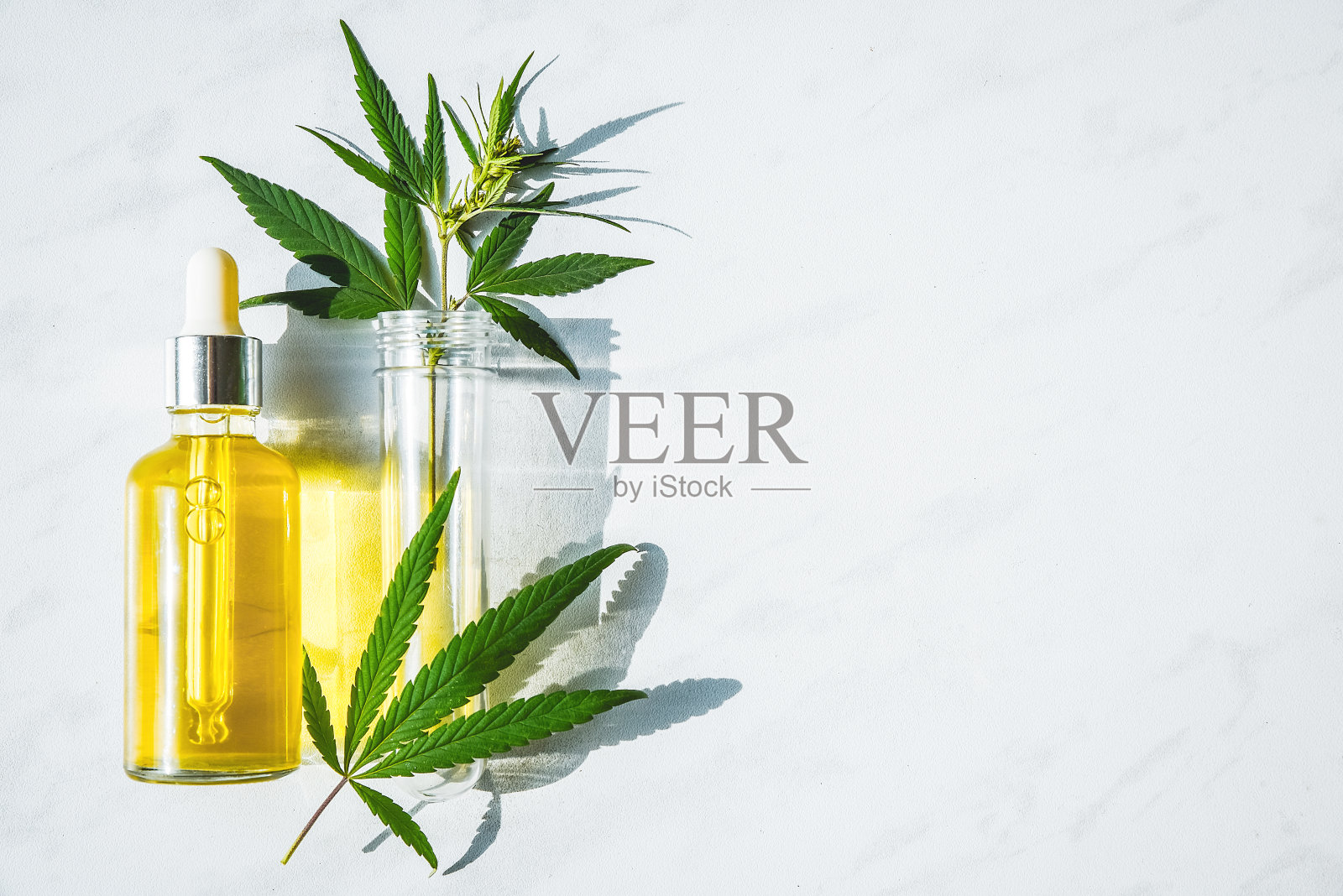 装有大麻油的玻璃瓶和一个装有大麻叶的试管放在大理石背景上。副本的空间。照片摄影图片
