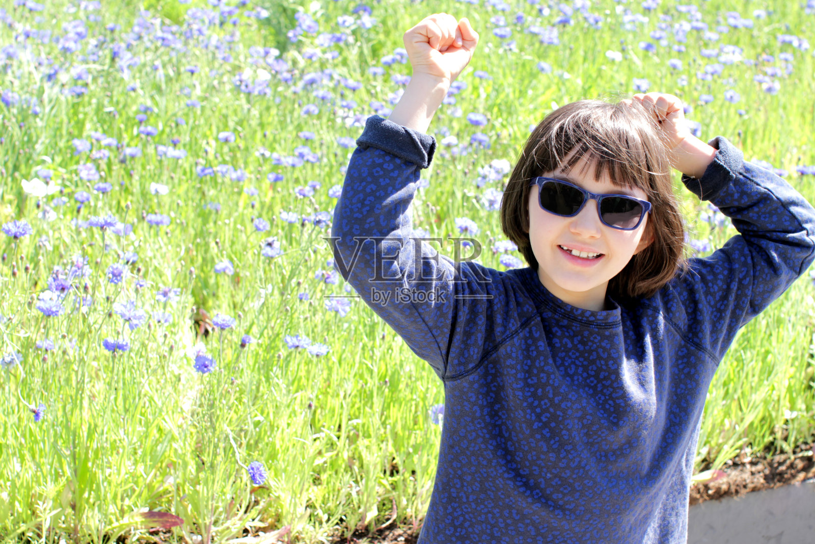 兴奋的年轻女孩戴着蓝色太阳镜在春天的矢车菊地照片摄影图片