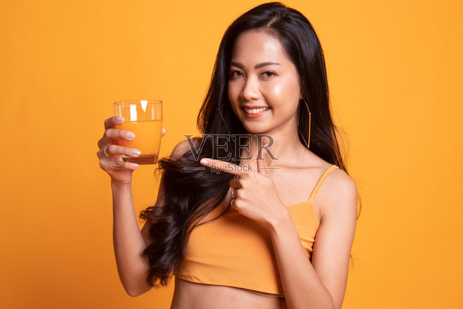 年轻的亚洲女人指着橙汁。照片摄影图片