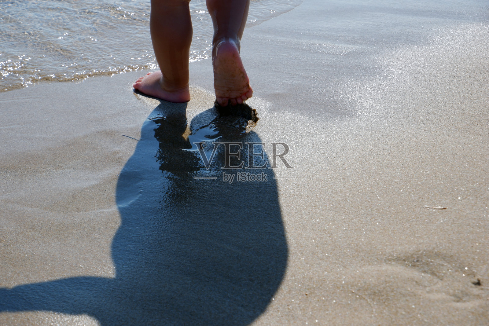 一个光着脚走向大海的男婴的特写镜头。照片摄影图片