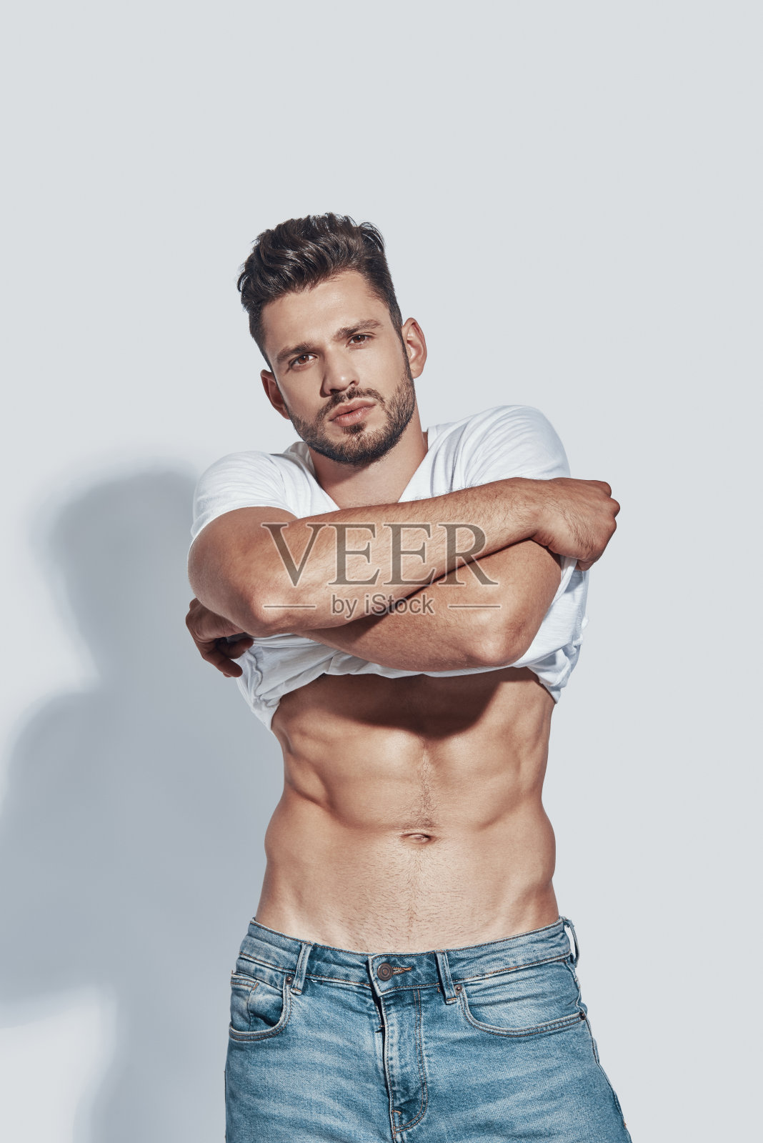 英俊的年轻人看着相机和脱衣服，而站在灰色的背景照片摄影图片