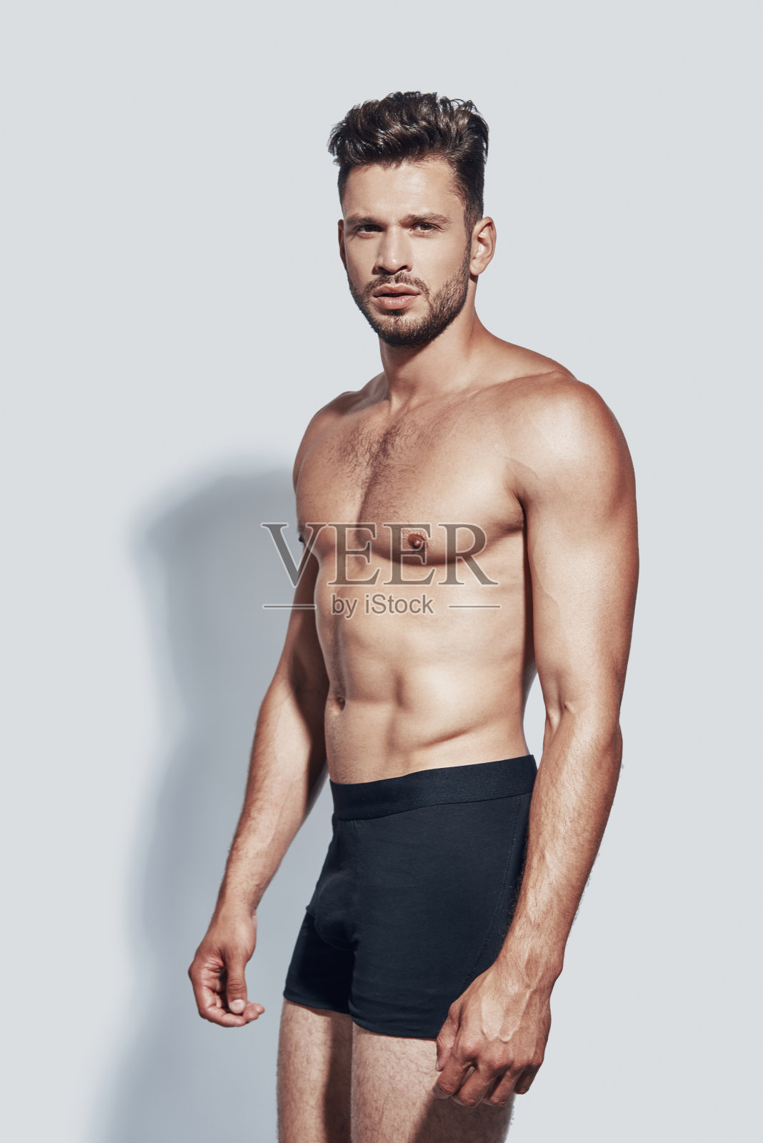 英俊年轻的赤膊男子看着相机，而站在灰色的背景照片摄影图片