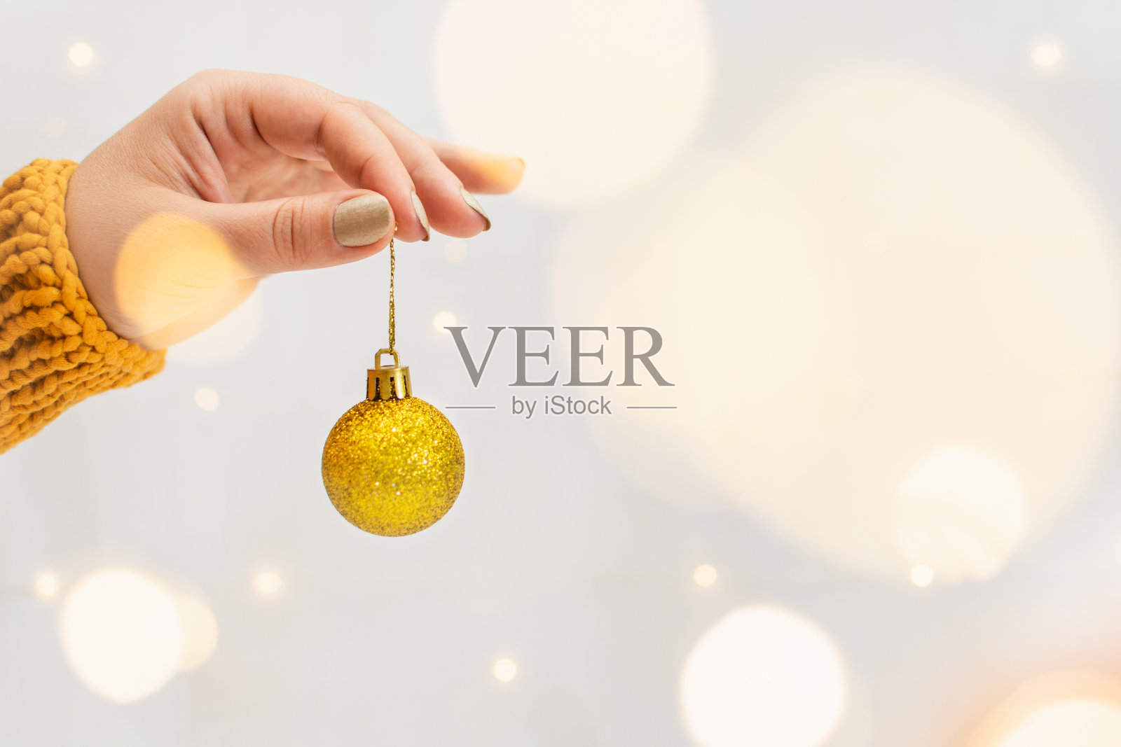女性的手拿着金色的圣诞树球与花环散景的背景照片摄影图片