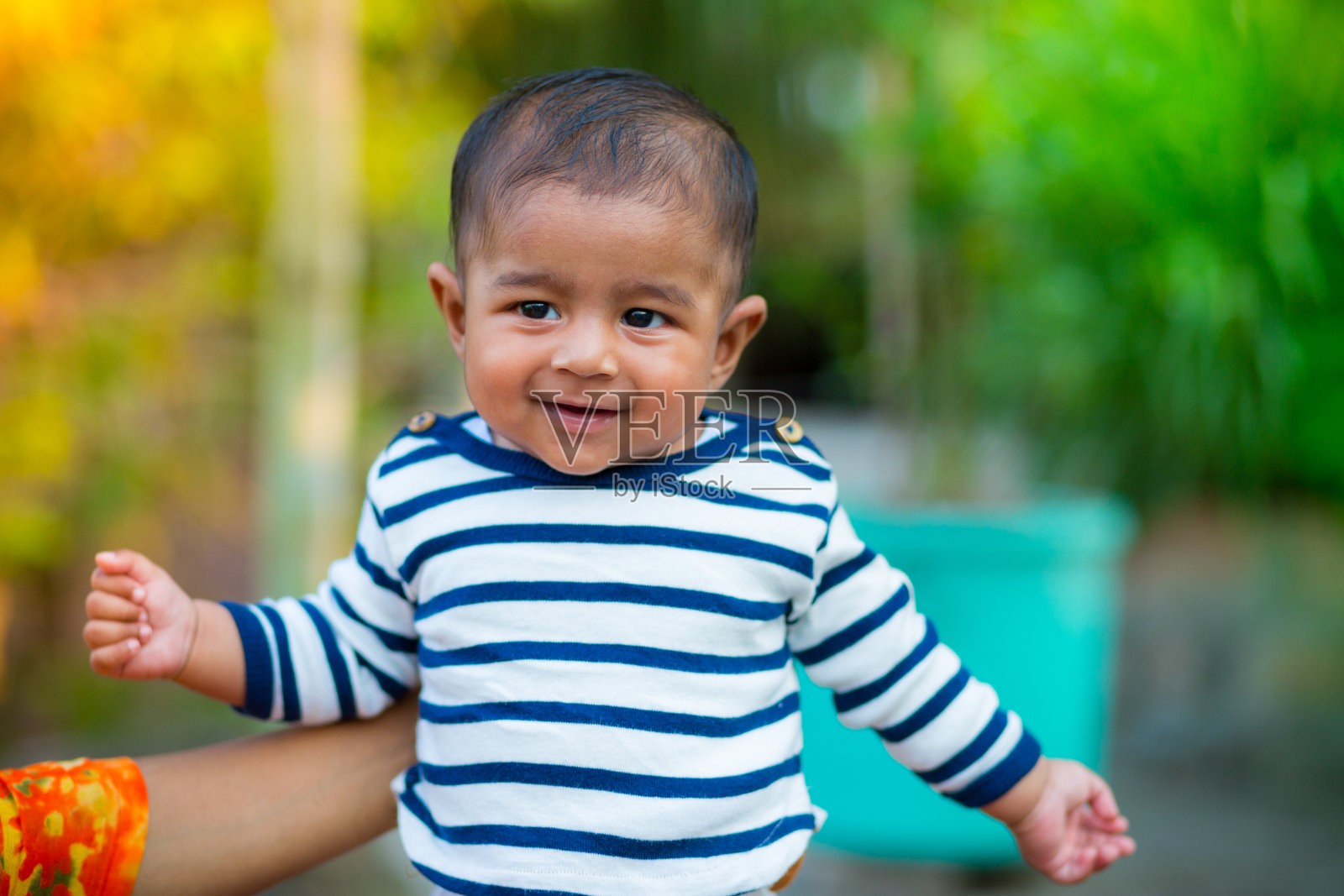 一个小男孩看着我，微笑着。着装是白色和海军蓝条纹的连衣裙。宝宝的拍摄。婴儿肖像。照片摄影图片