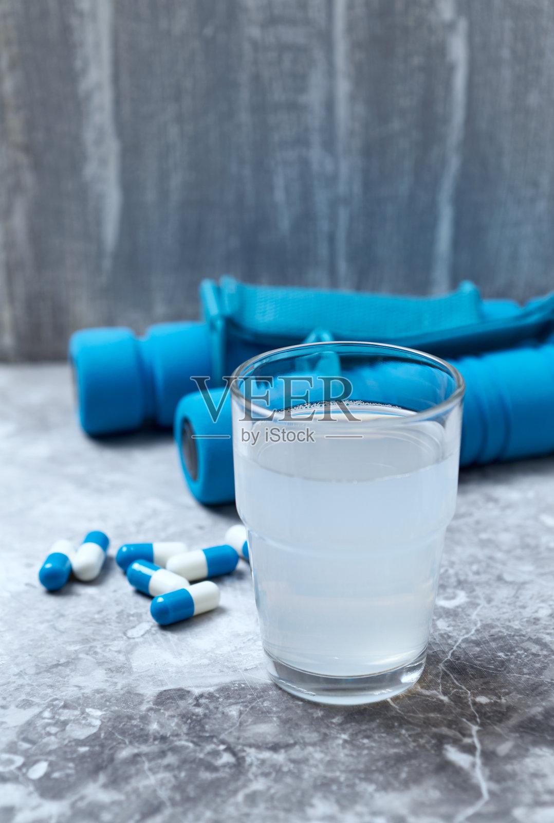 BCAA(氨基酸)饮料，肌酸胶囊和蓝色哑铃背景。运动营养。石头/木制背景。副本的空间。照片摄影图片