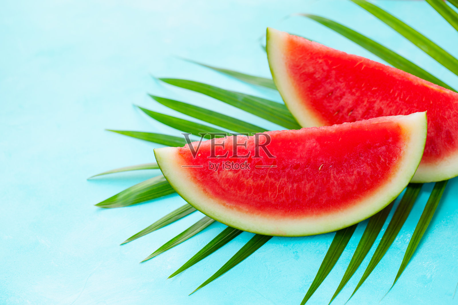 西瓜片在绿色的棕榈叶上。蓝色背景。副本的空间。照片摄影图片
