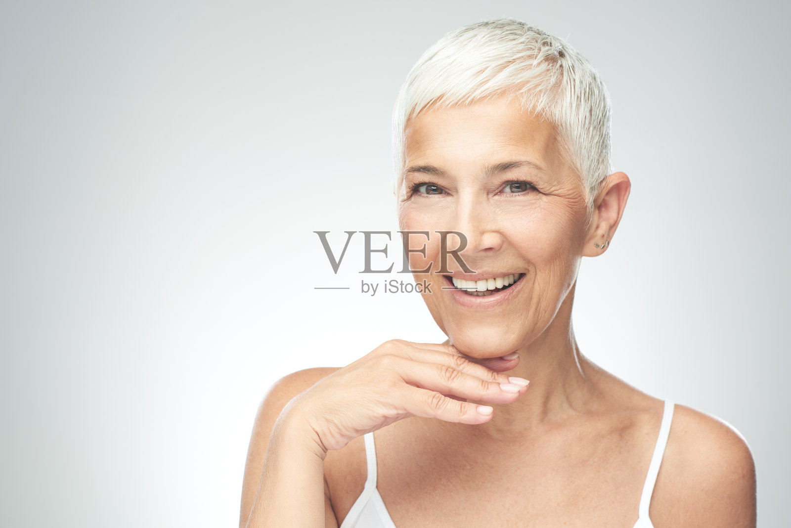 老妇人在灰色背景前摆姿势。照片摄影图片