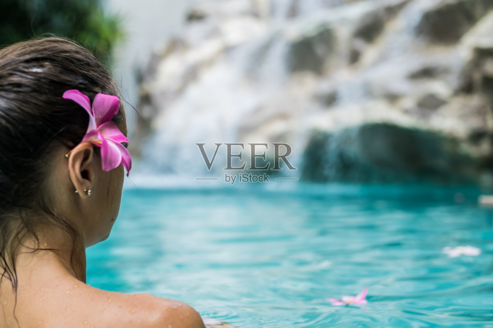 女孩在池中，瀑布附近，鸡蛋花在附近漂浮，水疗概念，放松近照片摄影图片