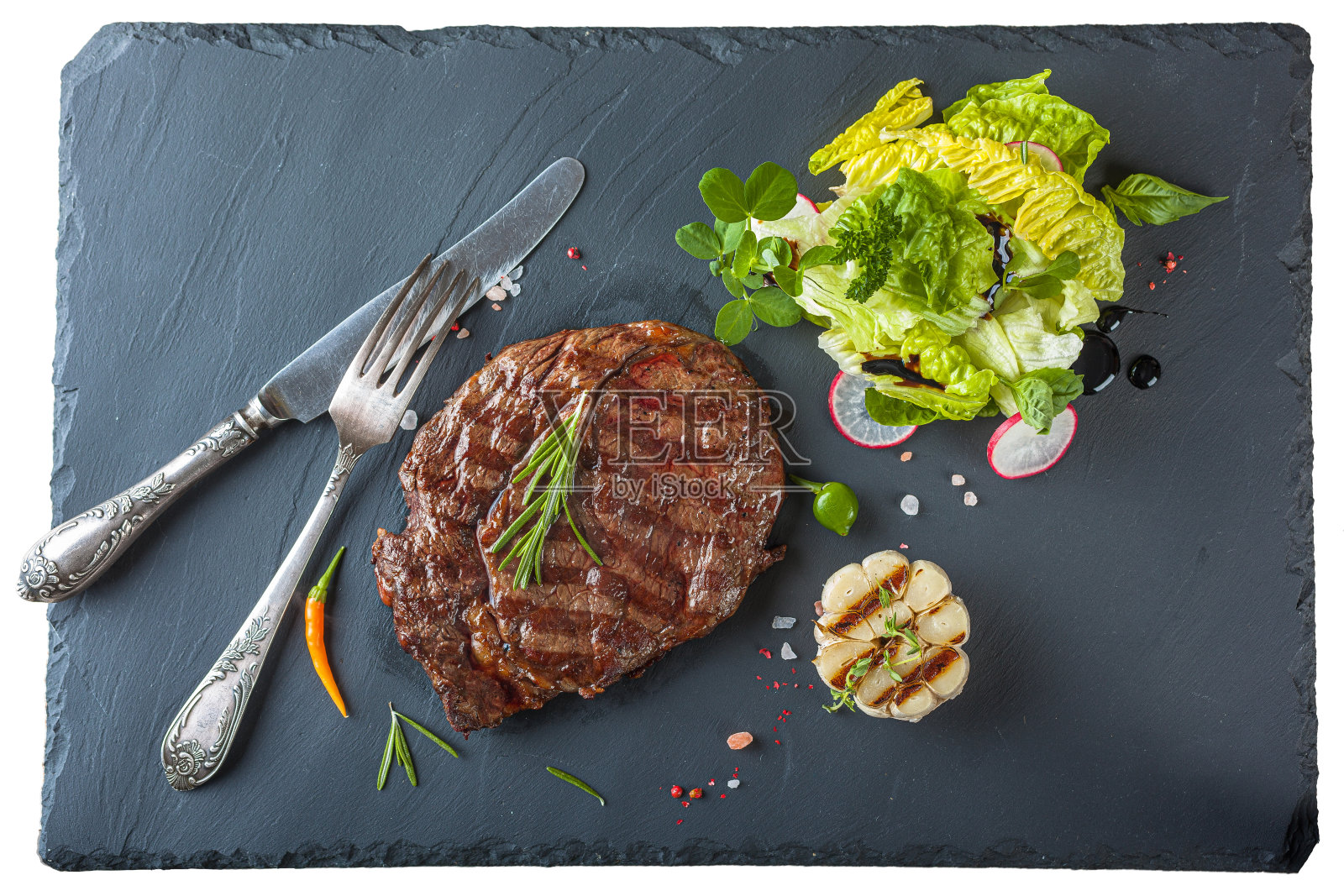 黑石板上的肋眼牛排配迷迭香和沙拉照片摄影图片