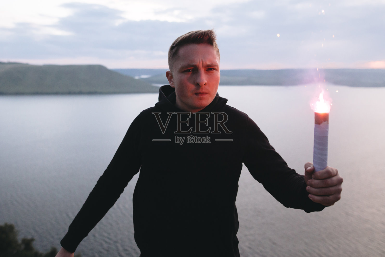 手持蓝色火炬的极端流氓，站在岩石山顶的傍晚与惊人的河的景色。大气的时刻。本空间照片摄影图片