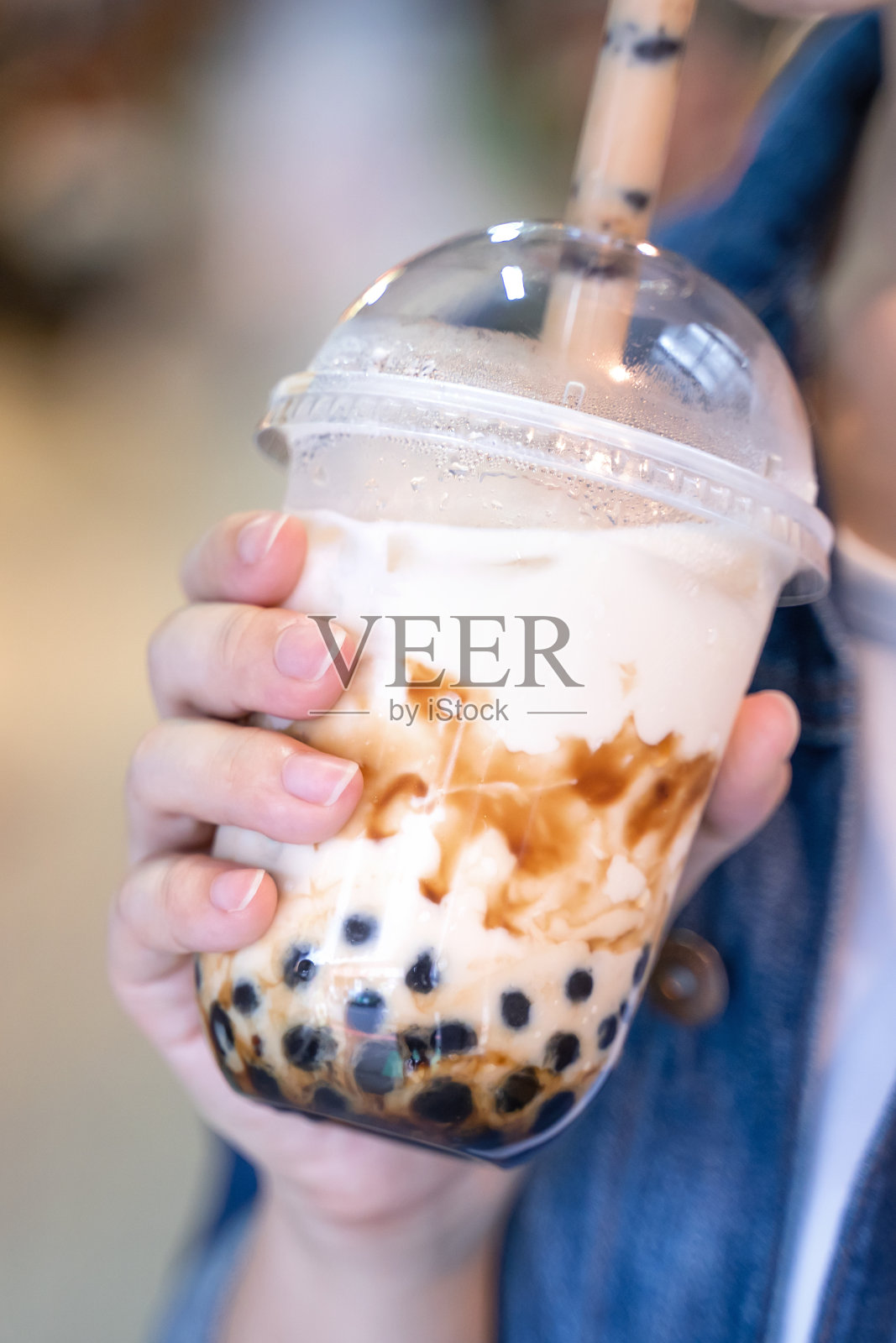 台湾夜市上，穿着牛仔夹克的小女孩正用玻璃吸管喝着红糖味的木薯珍珠奶茶。照片摄影图片