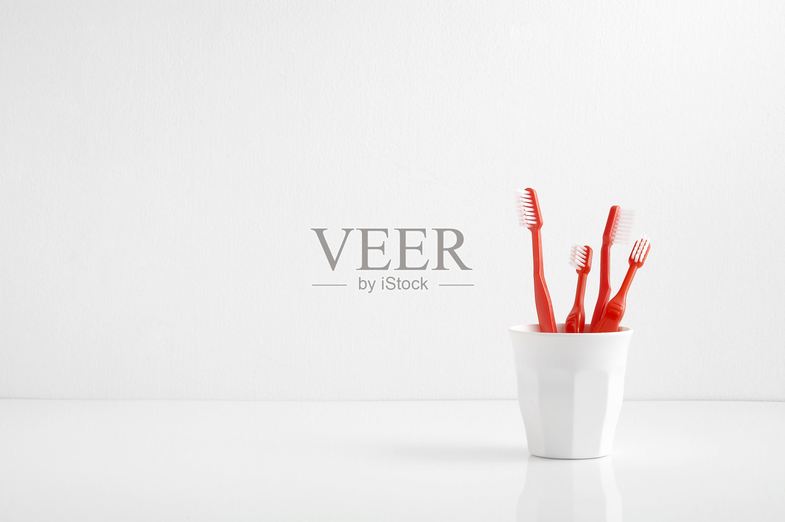 一组红色的牙刷放在一个塑料杯里，空出一个文字，牙刷放在浴室里照片摄影图片