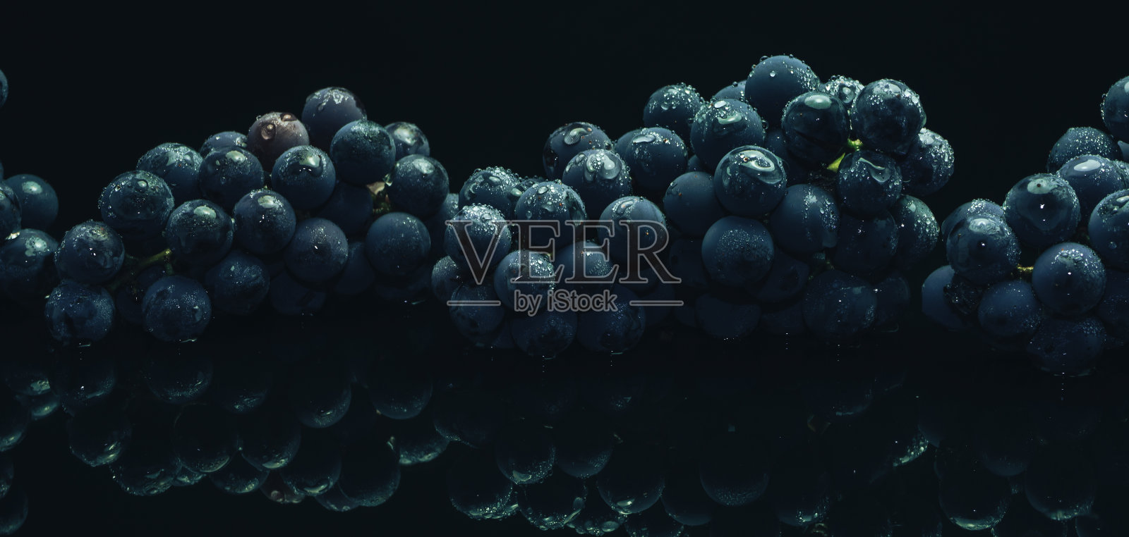靠近美丽的新鲜葡萄蓝葡萄在黑色玻璃桌子和黑暗的背景照片摄影图片