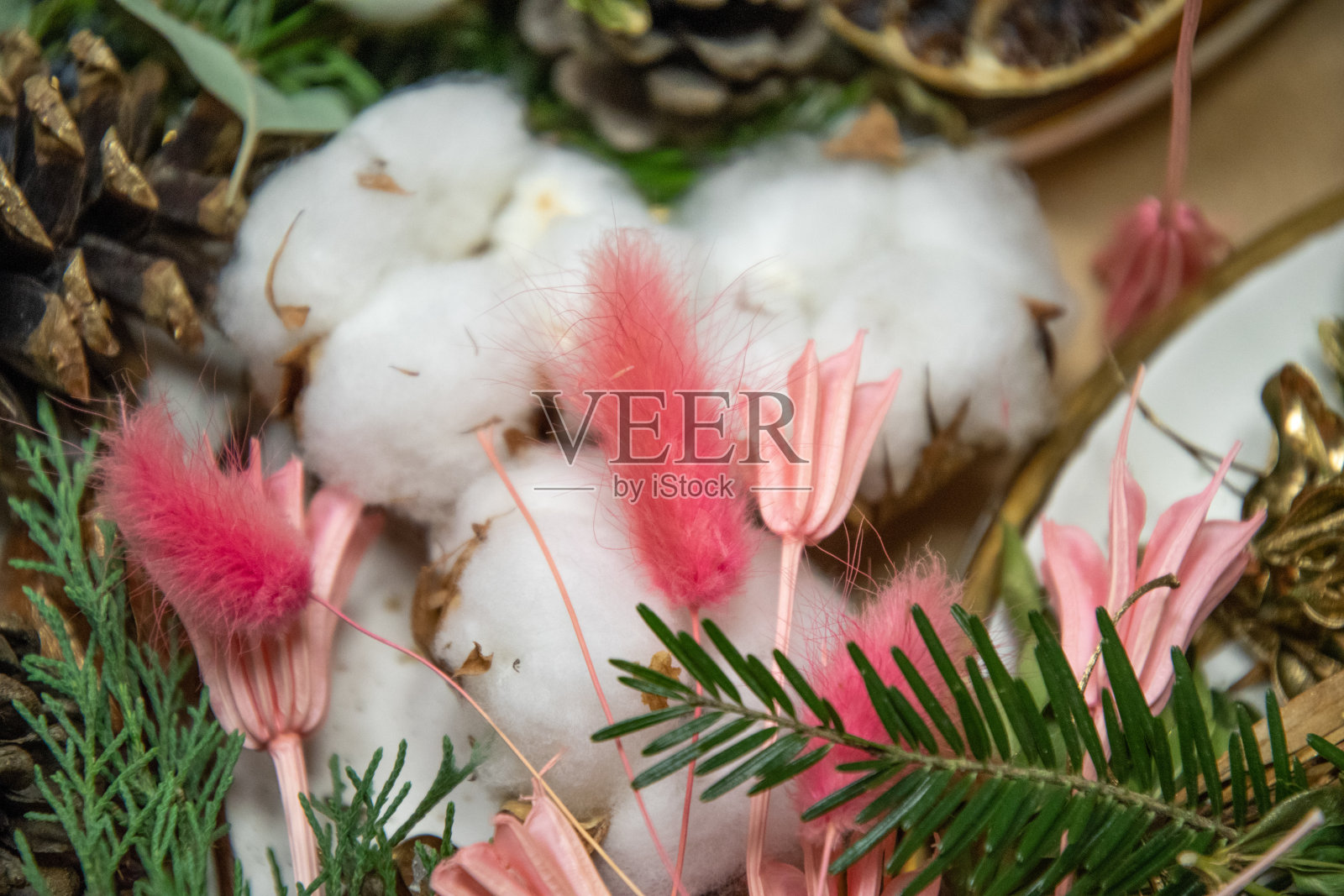手工桌上放着毛茸茸的粉红色花朵、白色的棉球和绿色的冷杉树枝。杂乱的工艺用品背景。制作手工装饰品的天然材料照片摄影图片