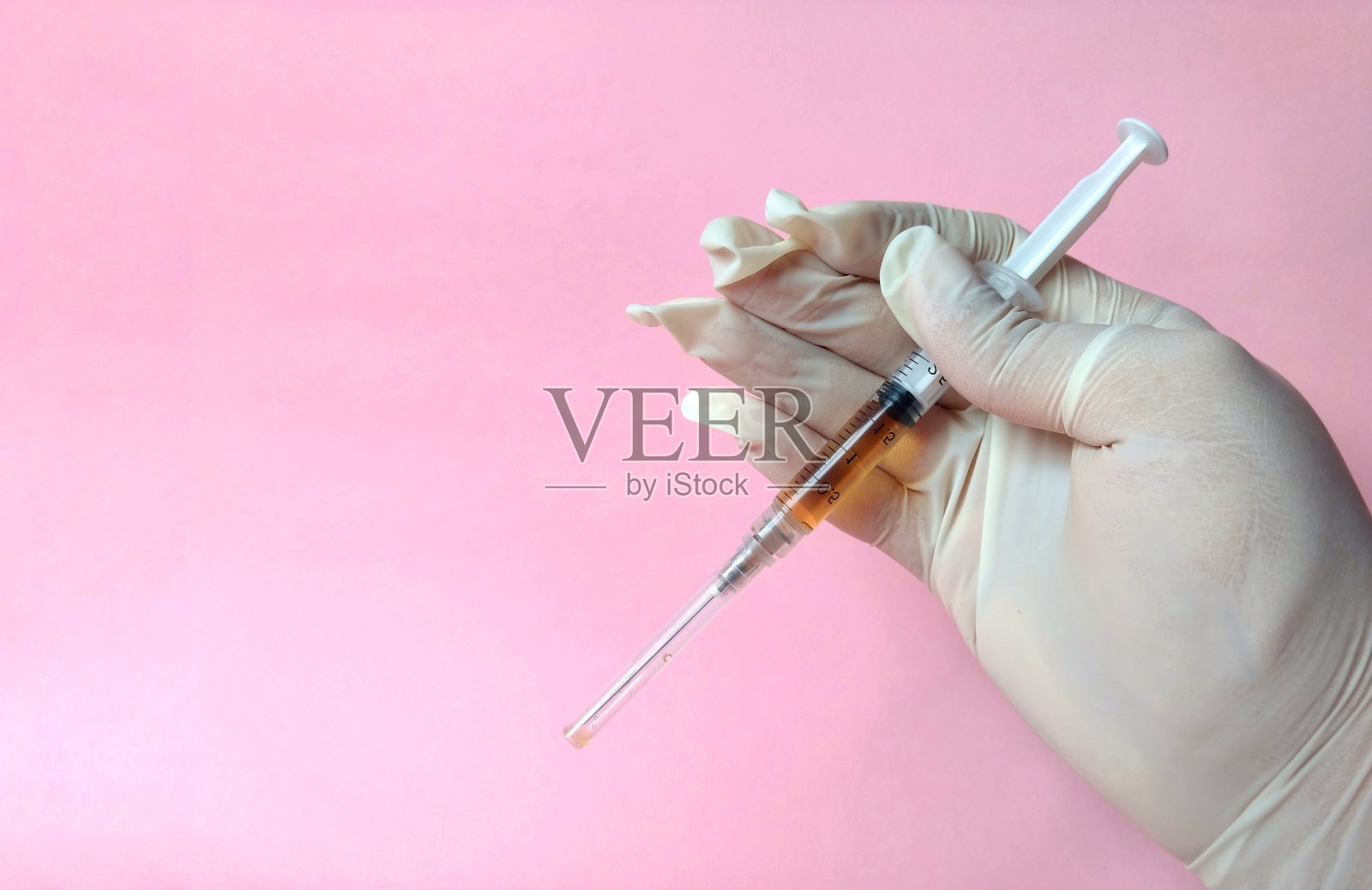 手与白色乳胶手套和注射器准备使用粉红色背景。医学的概念照片摄影图片