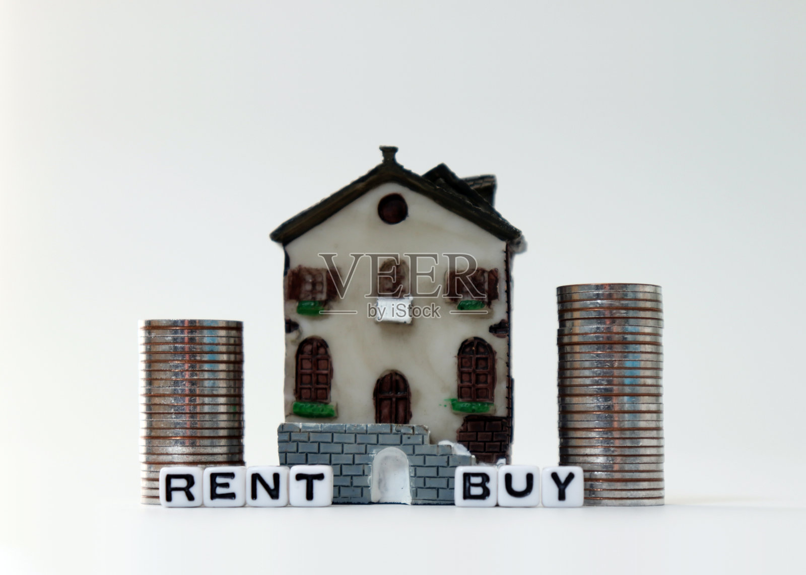 “买”和“租”的白色立方体上有一个微型房子。一个小房子和硬币堆。照片摄影图片