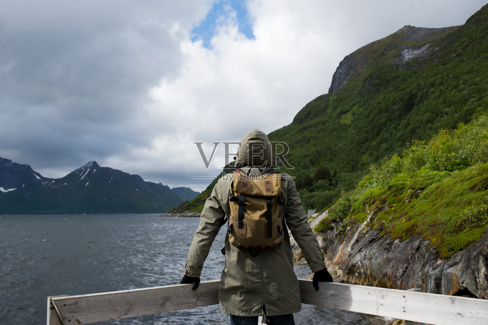 一个穿着夹克背着背包的男人正在欣赏挪威峡湾的美景。北方美丽的自然景观。令人惊叹的户外风景。旅行、探险、生活方式。罗弗敦群岛。斯堪的那维亚照片摄影图片