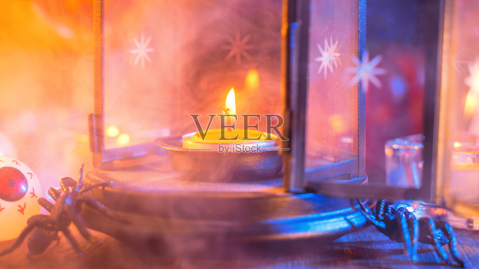 万圣节的概念，幽灵的装饰点燃蜡烛和蜡烛烛台与蓝色调烟雾周围的深色木桌。照片摄影图片