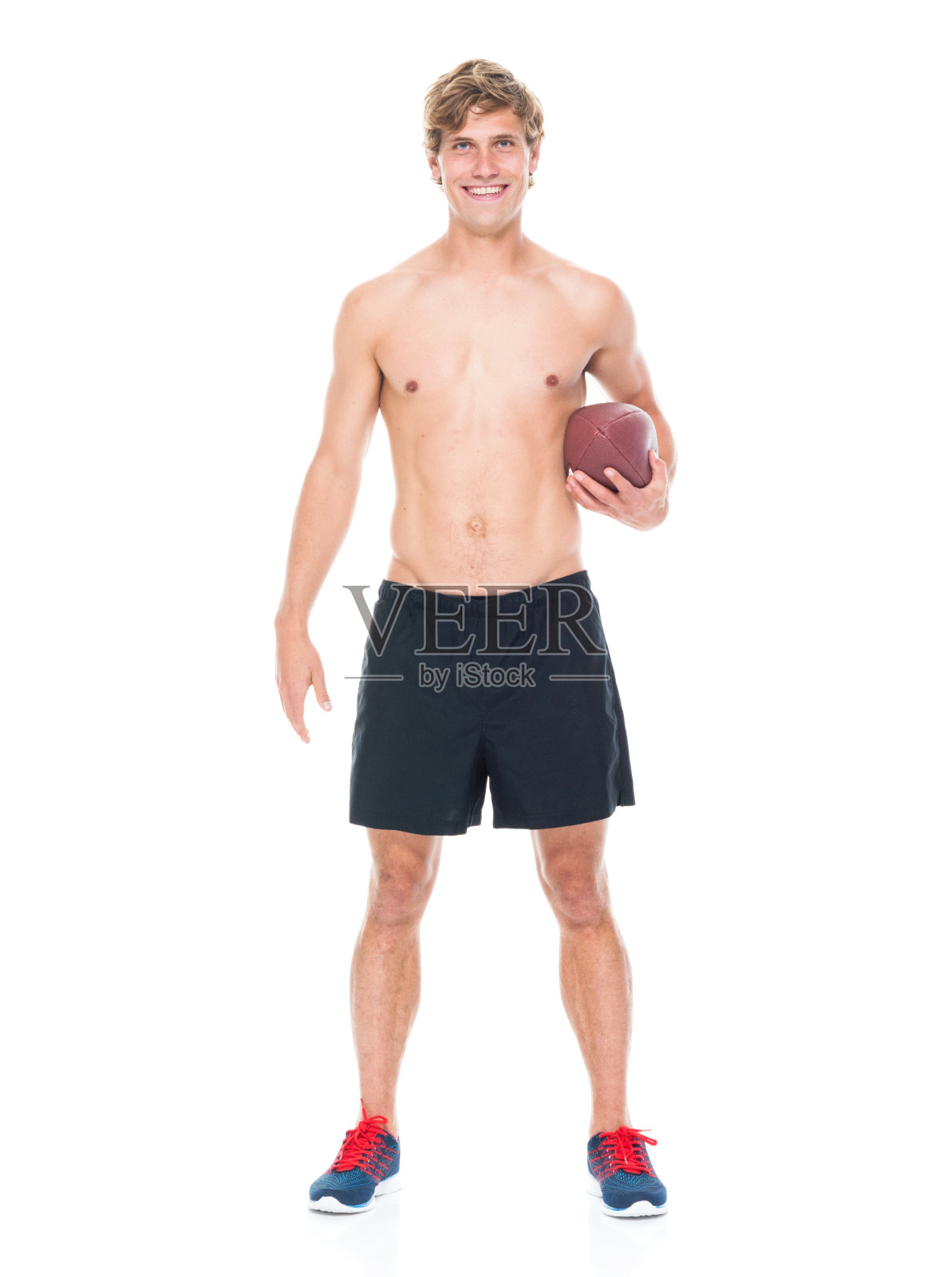 全身长度的20-29岁英俊的人白人男性/年轻男子运动员/运动员站在白色背景下，穿着运动服/跑步短裤/赤裸上身的短裤/性象征/微笑/快乐/开朗照片摄影图片