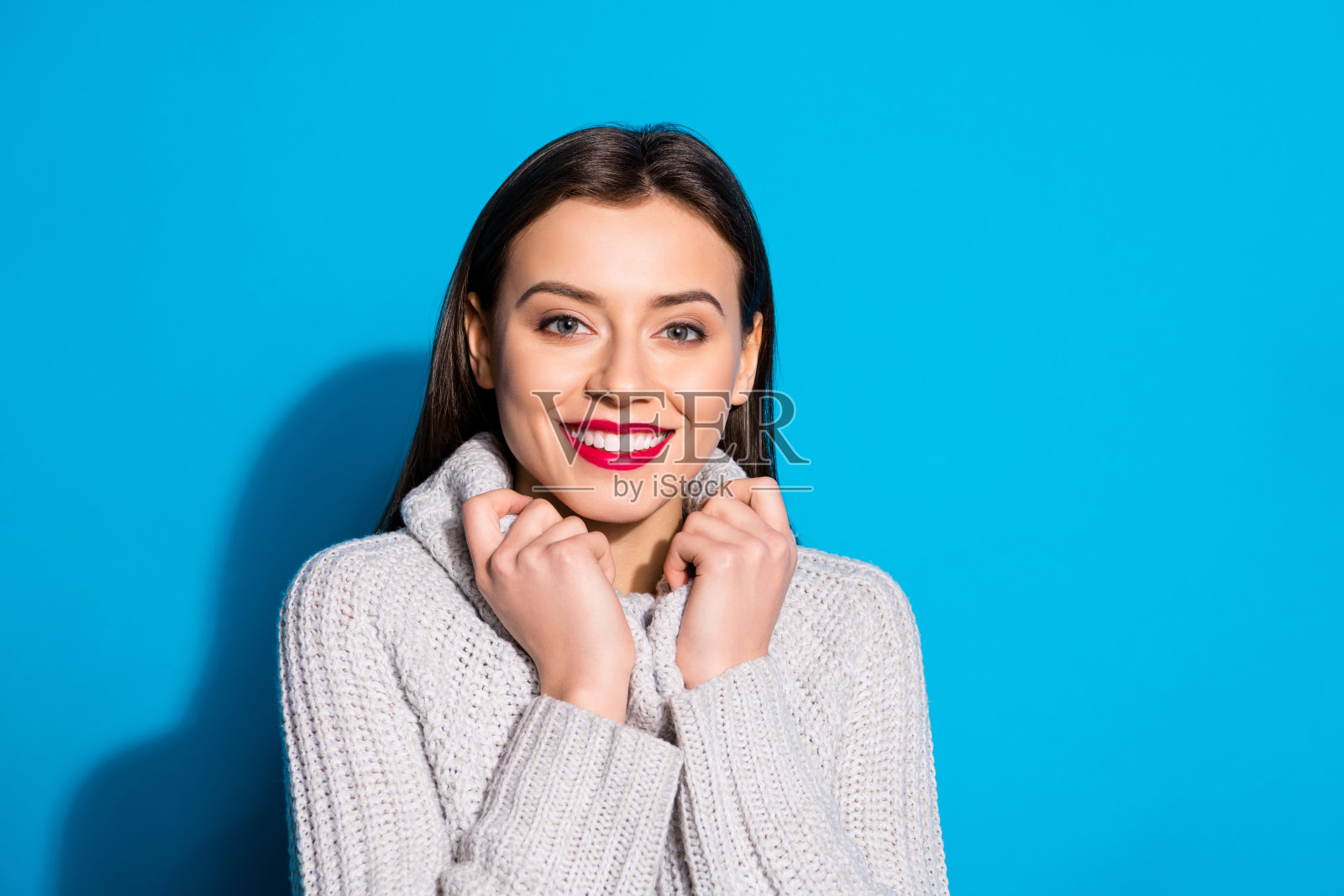 肖像迷人的女士触摸她的套头衫在相机孤立的蓝色背景微笑照片摄影图片