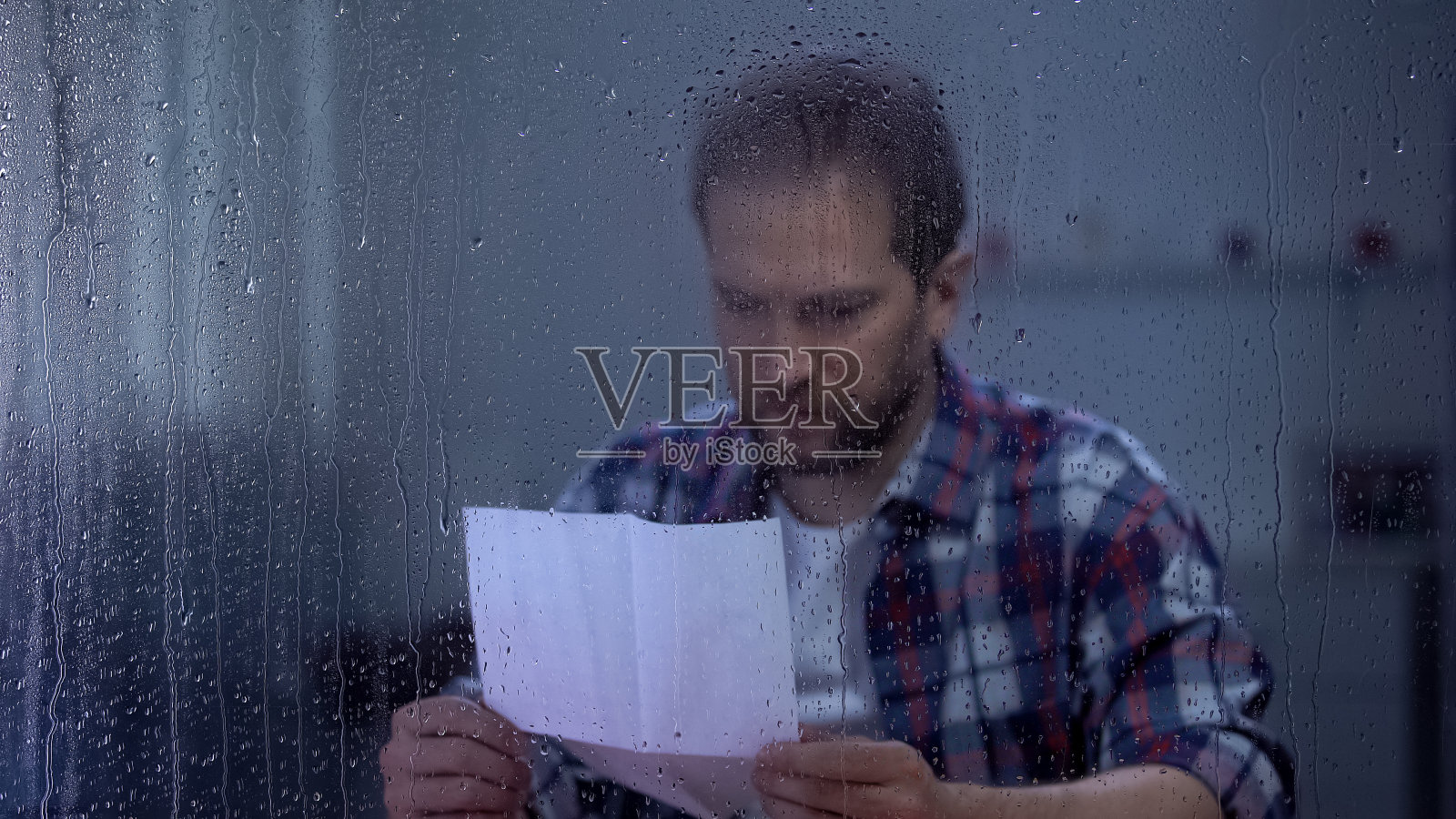 悲伤的男人躲在雨窗后读信，银行赊账逾期，贫穷照片摄影图片