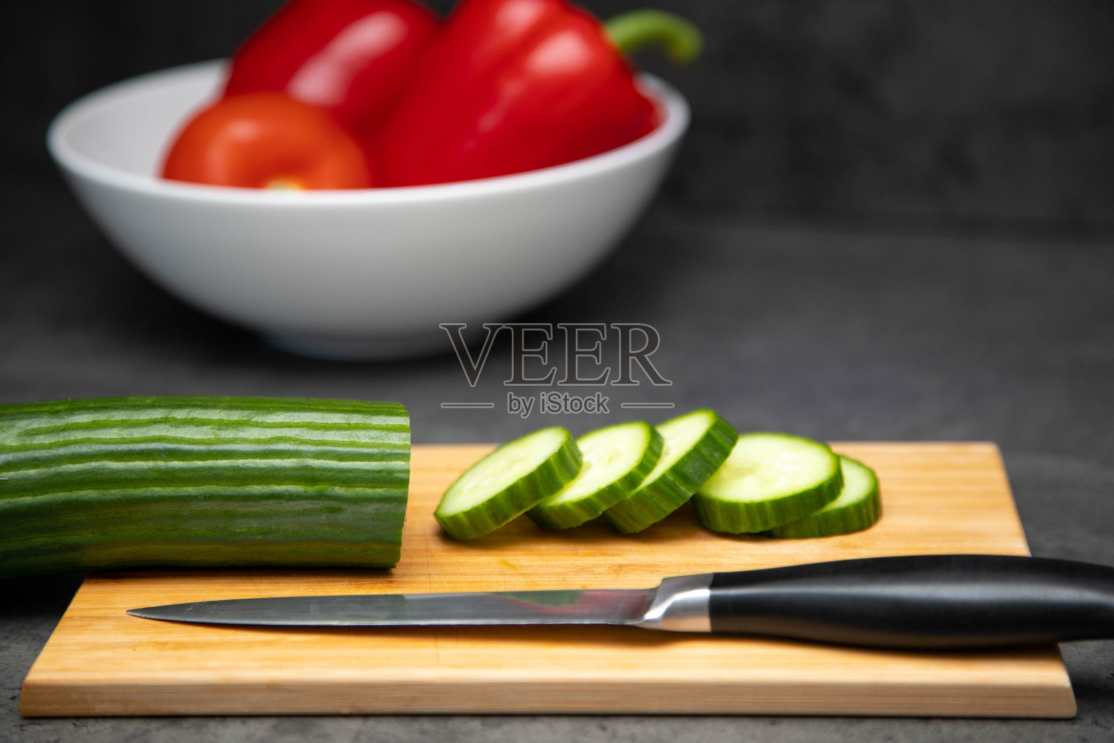 用刀把新鲜的黄瓜切成片，放在切菜板上，用陶瓷盘子盛蔬菜。照片摄影图片
