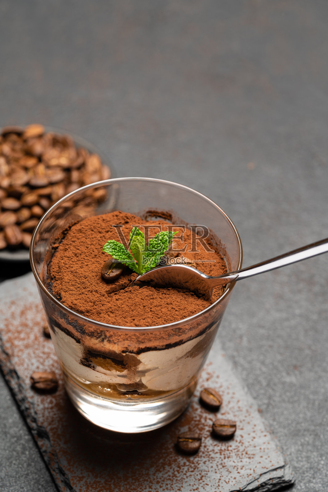 一份经典的提拉米苏甜点放在一个玻璃杯里，背景是黑色的混凝土照片摄影图片