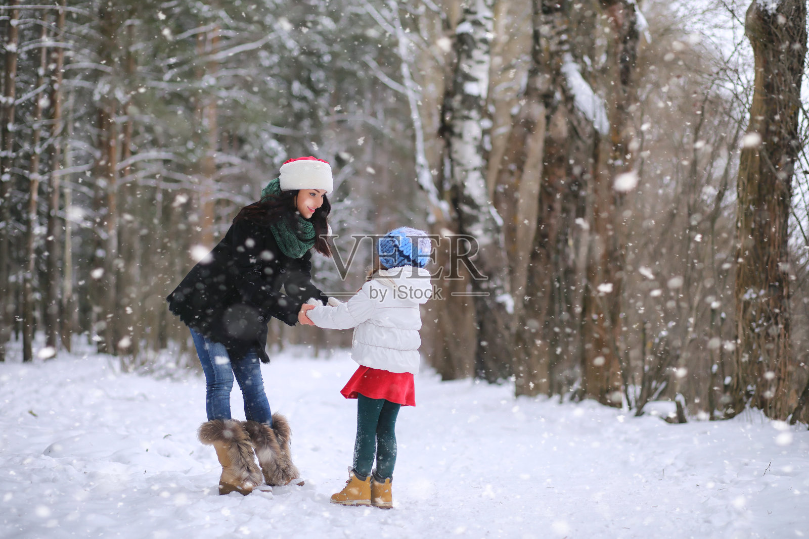 一个冬天的童话，一个年轻的母亲和她的女儿在森林里骑雪橇。新年前夕，公园里一个女孩坐在雪橇上，手里拿着礼物。两姐妹在新年公园散步，带着礼物坐雪橇。照片摄影图片