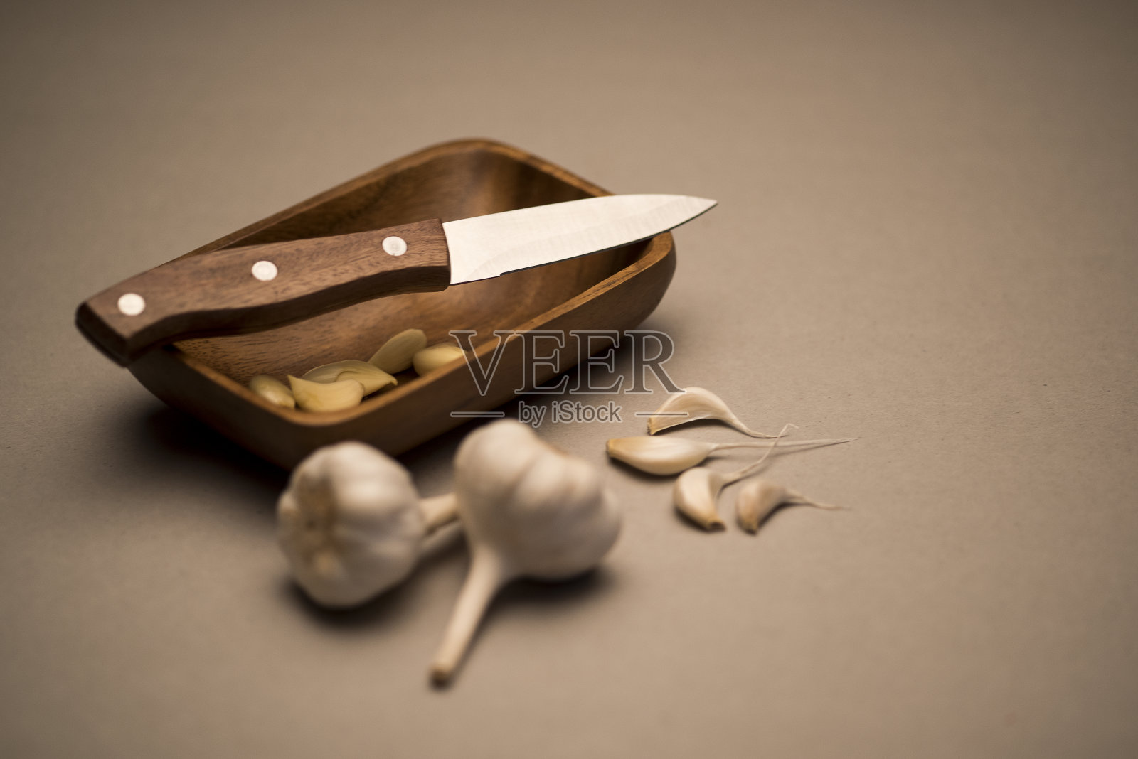 把大蒜和刀放在一个木盘子里，上面放着几颗剥了皮的大蒜荚照片摄影图片