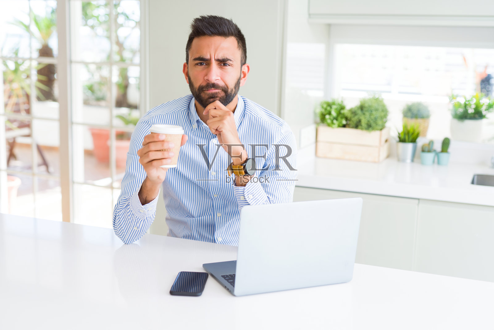 英俊的西班牙裔男人使用笔记本电脑工作，喝着一杯咖啡，思考问题，感到非常困惑照片摄影图片