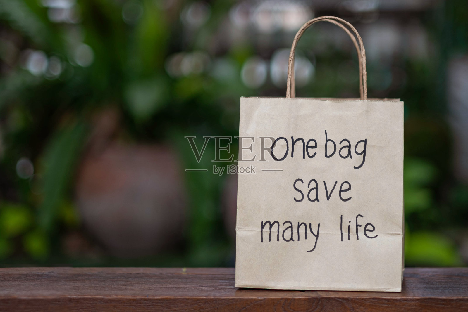 棕色的可回收纸购物袋放在一张木桌上，背景是一棵绿树。对于用于竞选活动的背景图像，不要使用塑料袋。照片摄影图片
