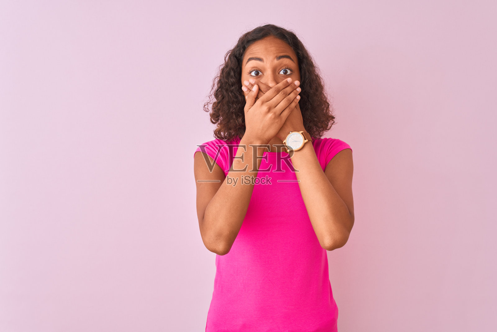 年轻的巴西女子穿着t恤站在孤立的粉色背景震惊了，错误地用手捂住了嘴。秘密的概念。照片摄影图片