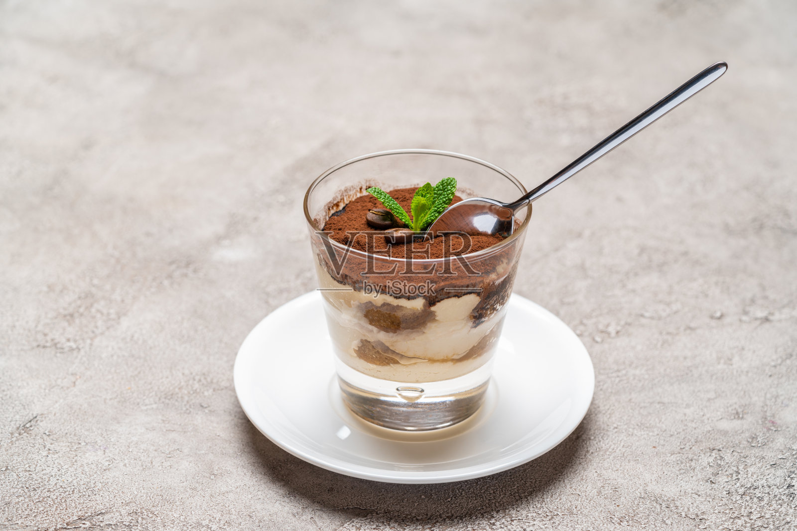 一份经典的提拉米苏甜点放在玻璃杯里，背景是混凝土照片摄影图片