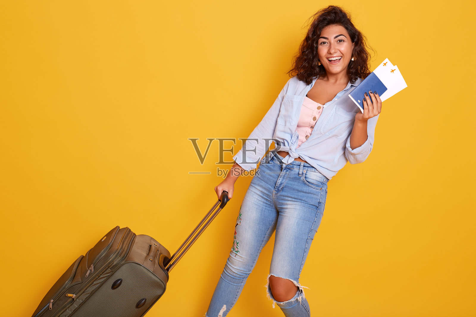 近距离拍摄了一幅欧洲高加索女性的肖像，她穿着时髦的衣服，提着装有机票和文件的手提箱，梦想着飞行和旅行，在黄色的背景下与世隔绝。照片摄影图片