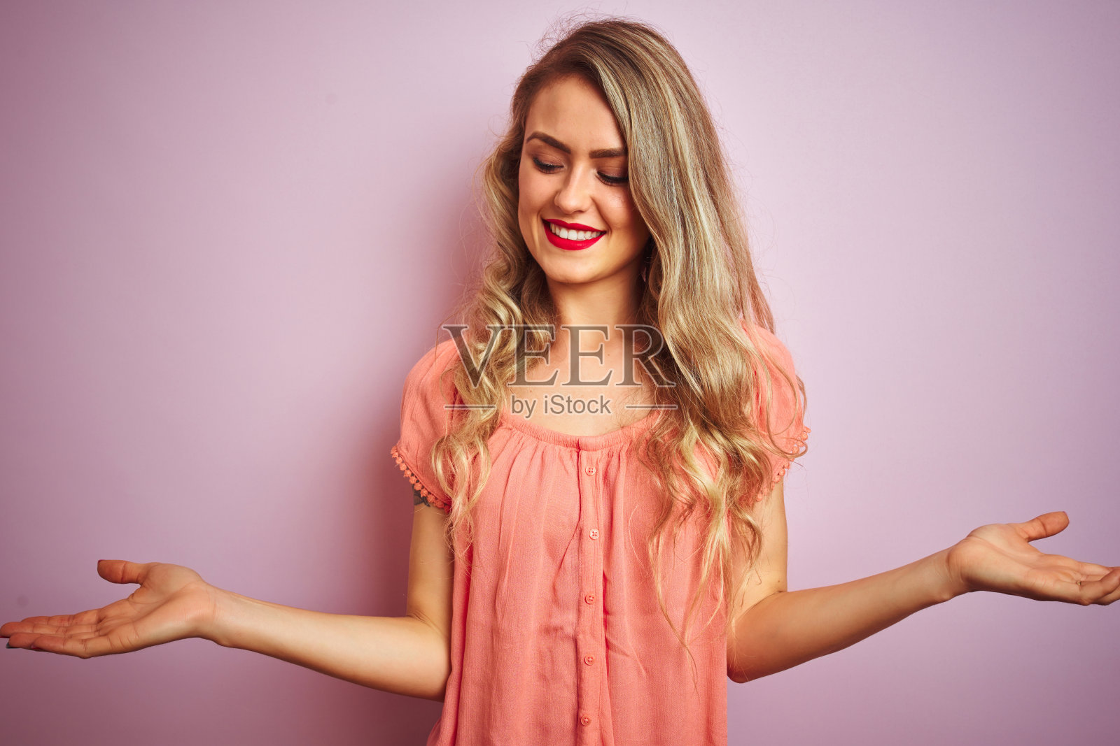 年轻美丽的女人穿着t恤站在粉红色孤立的背景微笑显示双手张开的手掌，呈现和广告比较和平衡照片摄影图片