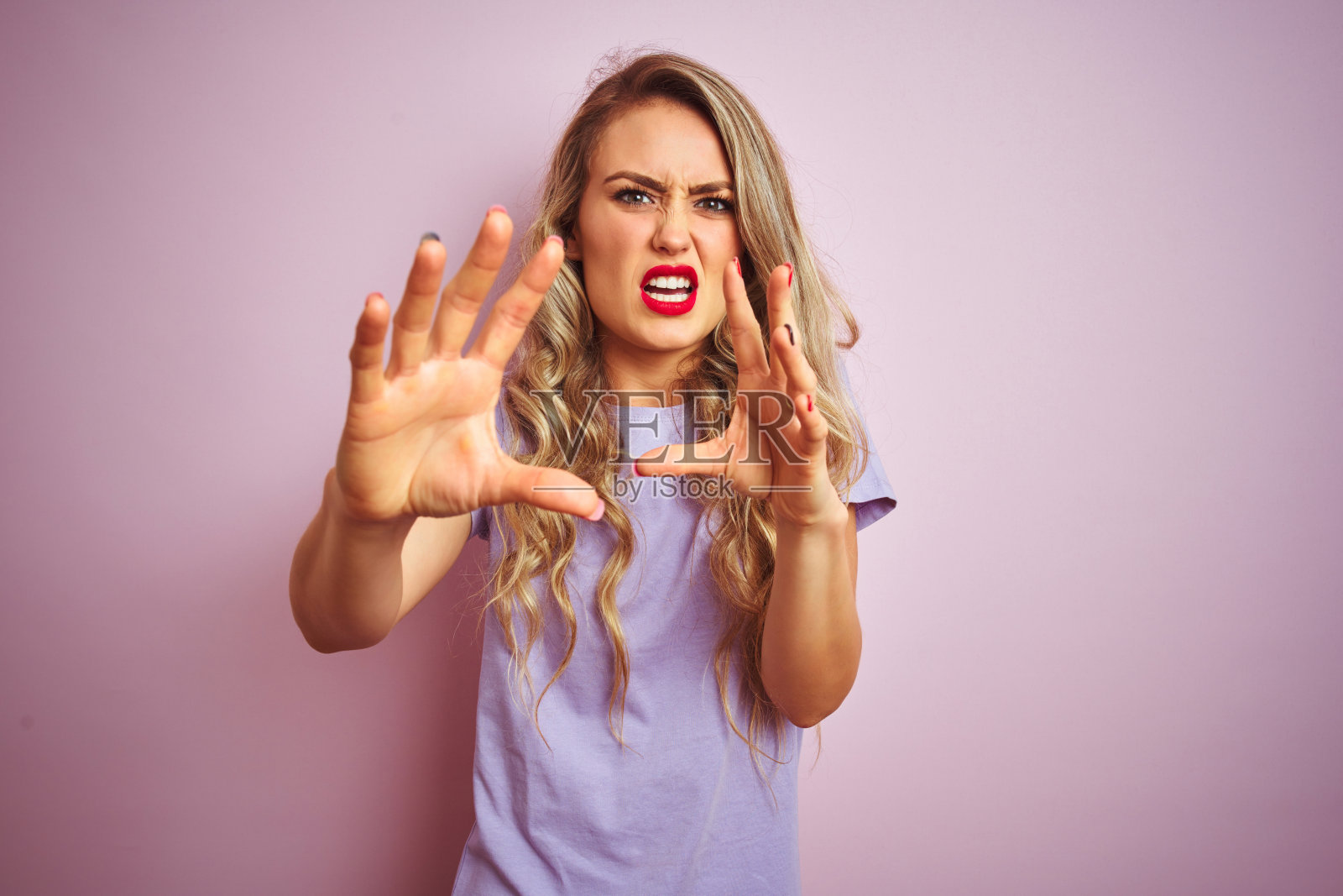 年轻美丽的女子穿着紫色的t恤站在粉色孤立的背景害怕和恐惧的表情停止手势与手，在震惊中大叫。恐慌的概念。照片摄影图片