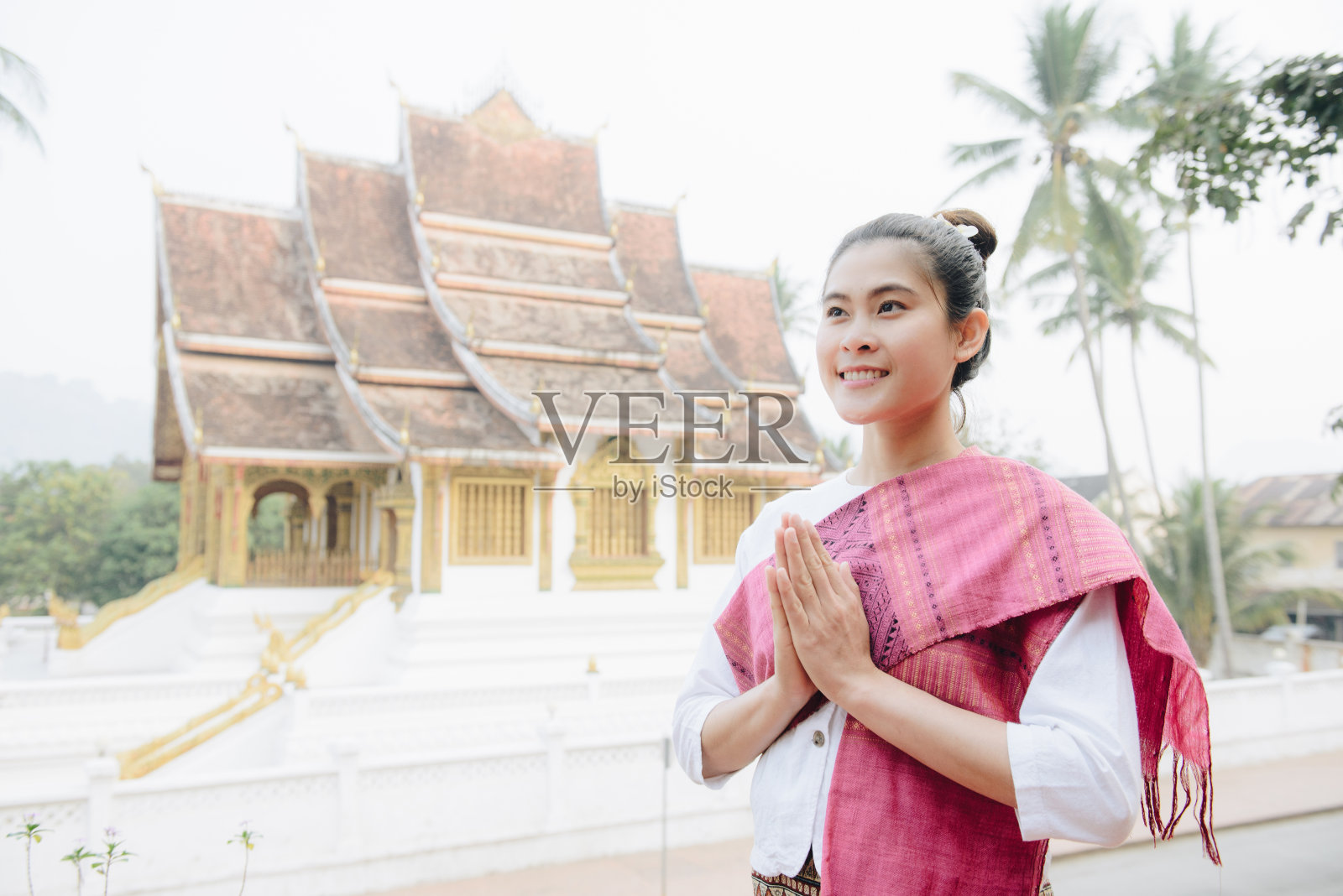 在老挝中北部的联合国教科文组织世界遗产琅勃拉邦皇宫前，一名身穿老挝传统服饰的亚洲妇女的肖像，正在表演问候。照片摄影图片