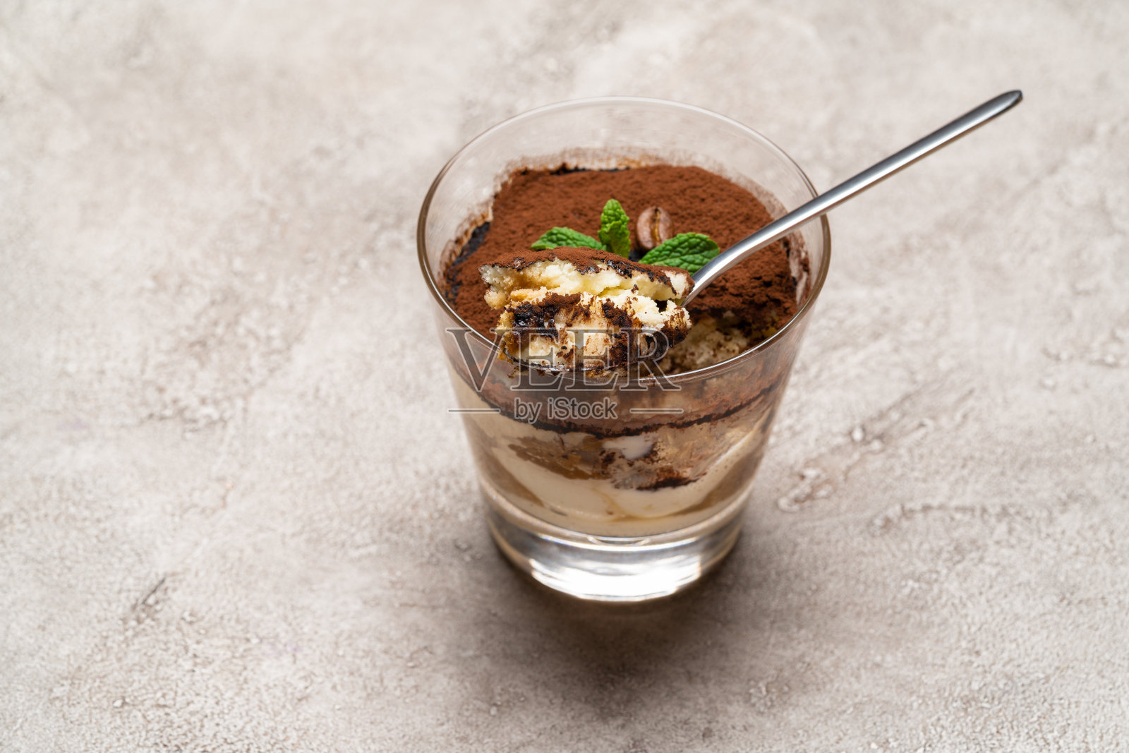 一份经典的提拉米苏甜点放在玻璃杯里，背景是混凝土照片摄影图片