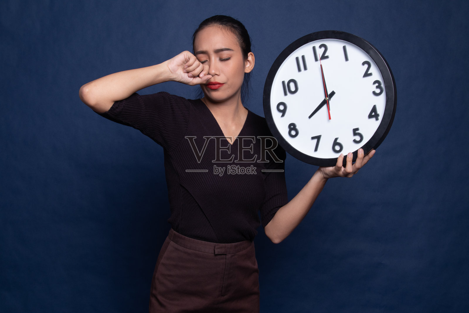 睡眼惺忪的年轻亚洲女人早上拿着钟。照片摄影图片